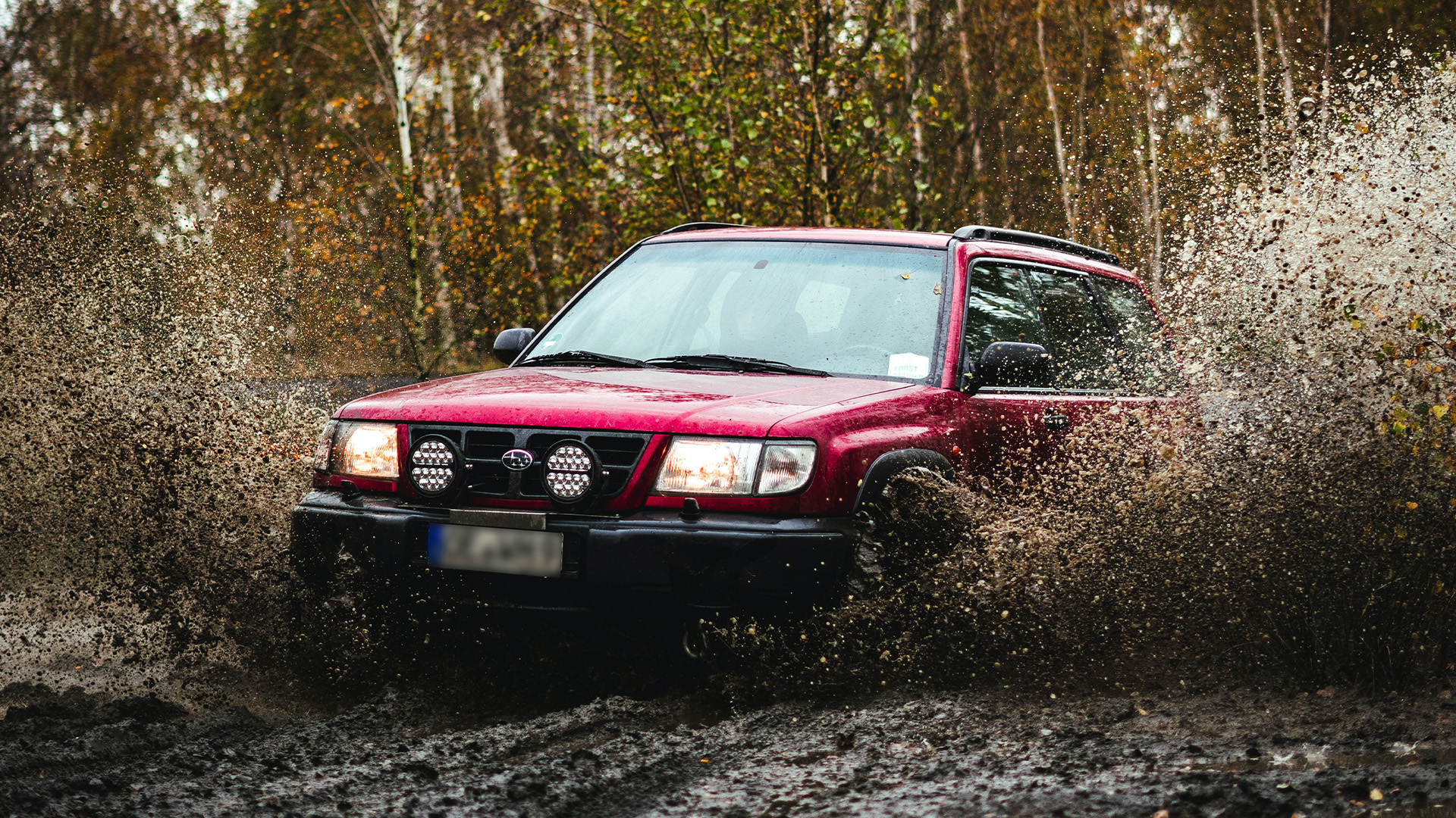 red Subaru spraying mud into the air